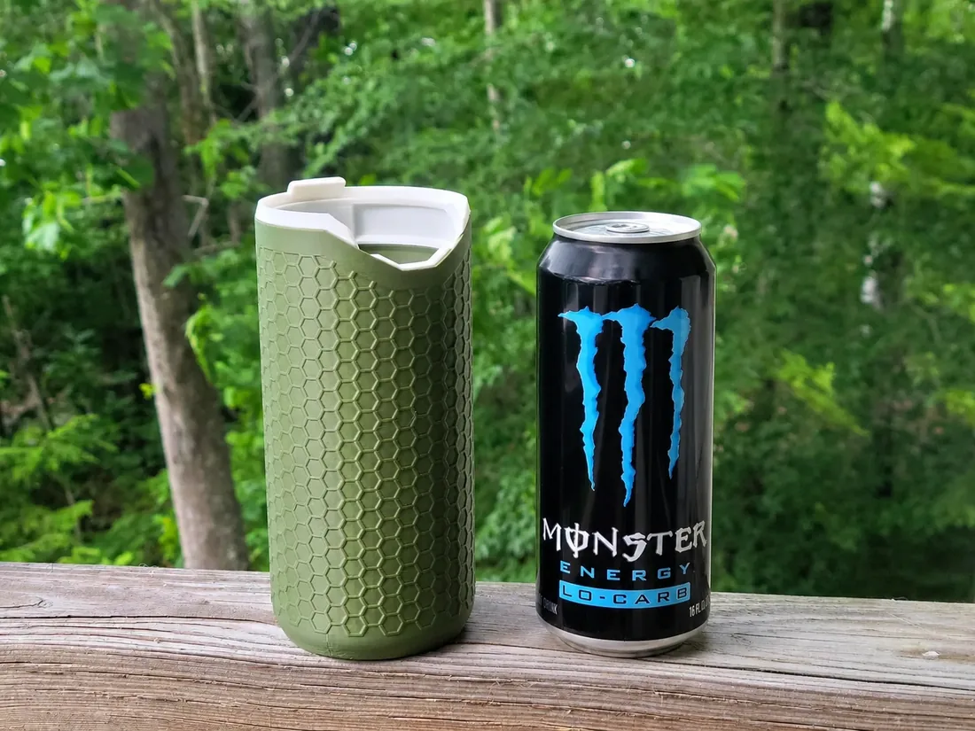 Porta-lata térmico PopTop Koozie verde ao lado de uma lata de Monster de 500 ml